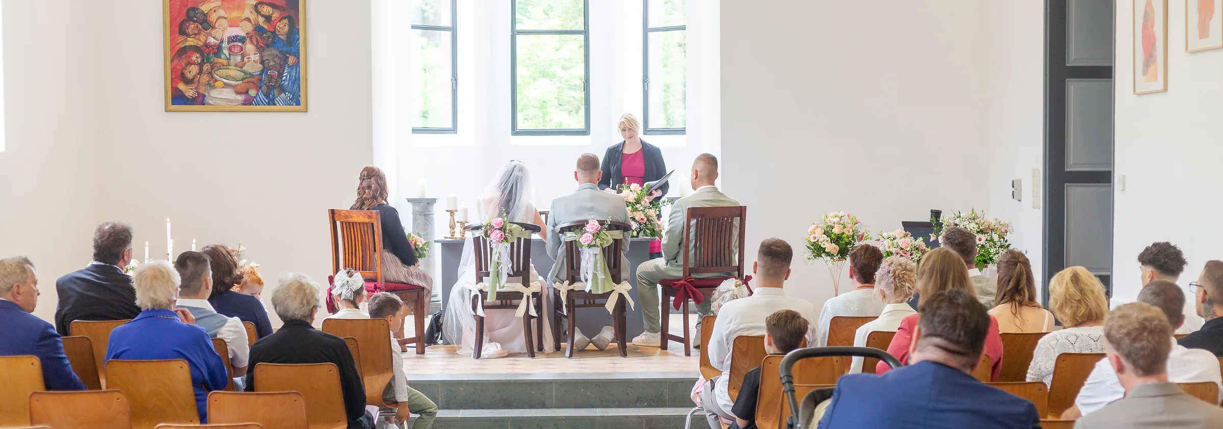 Eine freie Trauung mit Hochzeitspaar, Traurednerin und Gästen in einem hellen Saal.