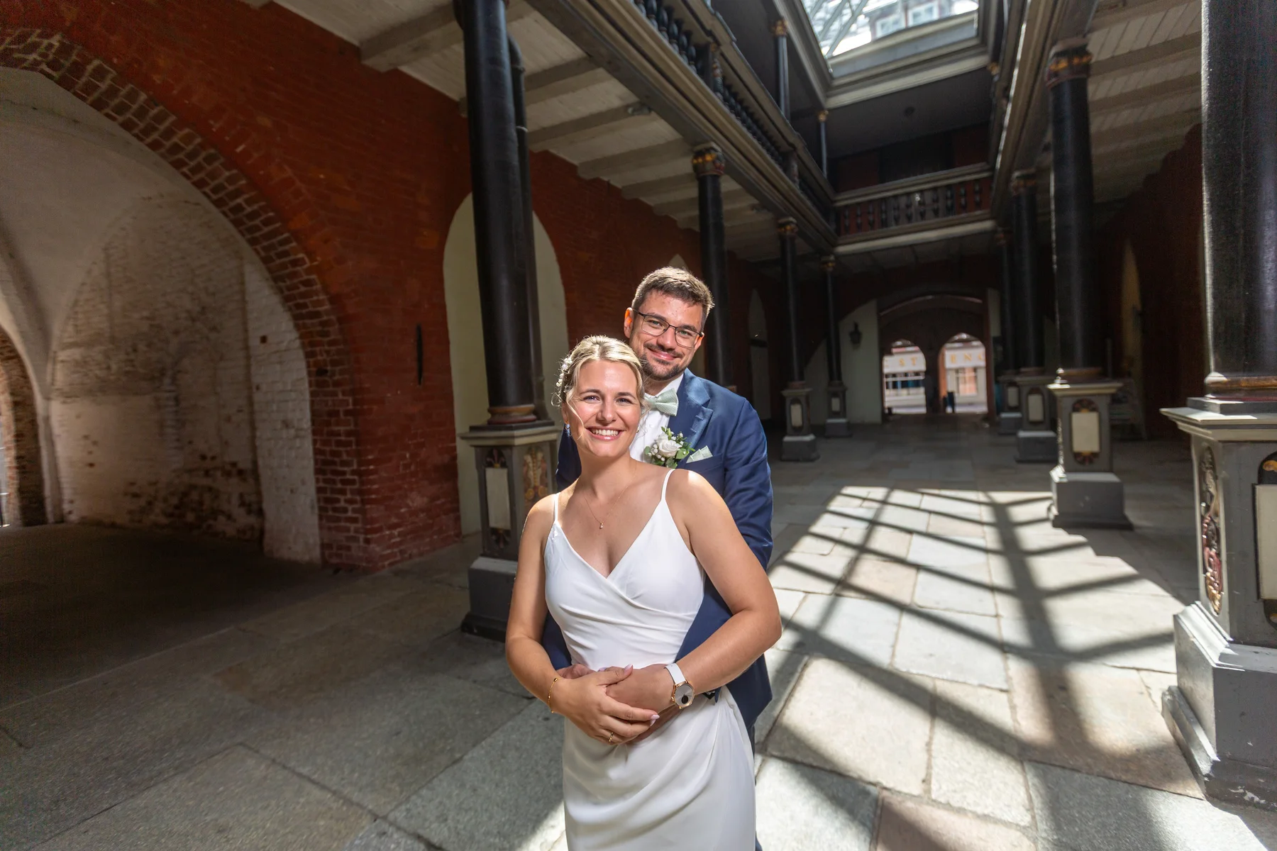 Das Hochzeitspaar lächelt gemeinsam in der Säulenhalle des historischen Rathauses.