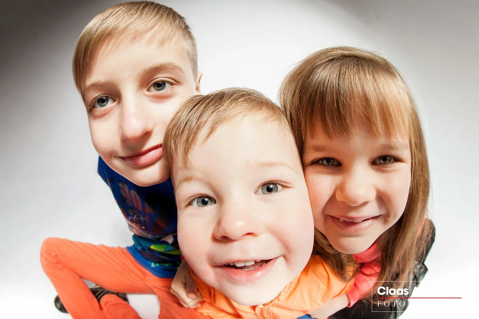 Drei Kinder schauen gemeinsam aus kurzer Entfernung in die Kamera.